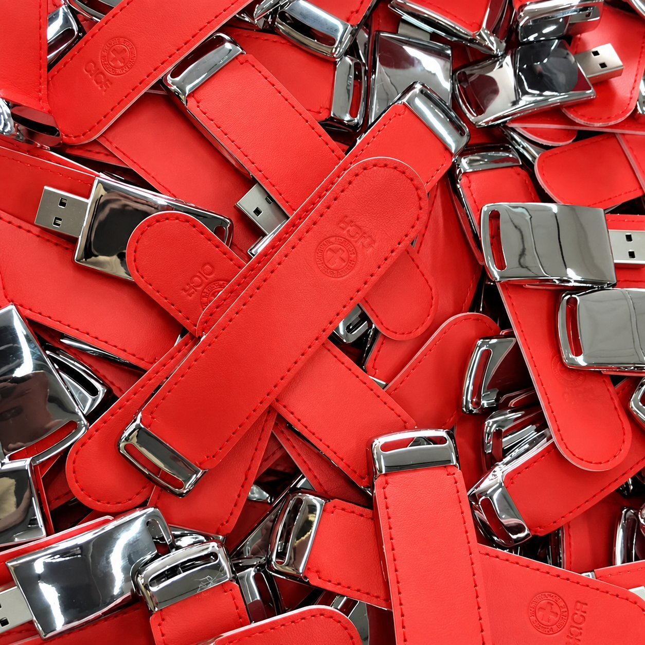 A pile of red leather USB flash drives with chrome-finished end caps and a small embossed logo on the body, illustrating a premium custom-mold leather USB style typically ordered as a luxury corporate gift or executive giveaway.