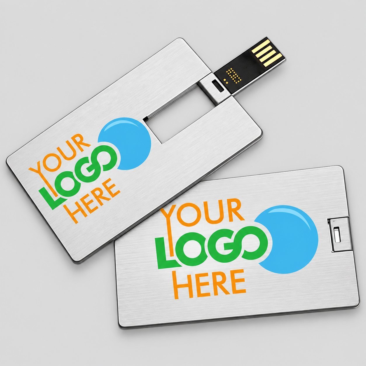 Two slim silver credit-card USB drives printed with a YOUR LOGO HERE placeholder graphic in green, blue, and orange, illustrating the credit-card form factor with a large flat printing surface for full-color branding.