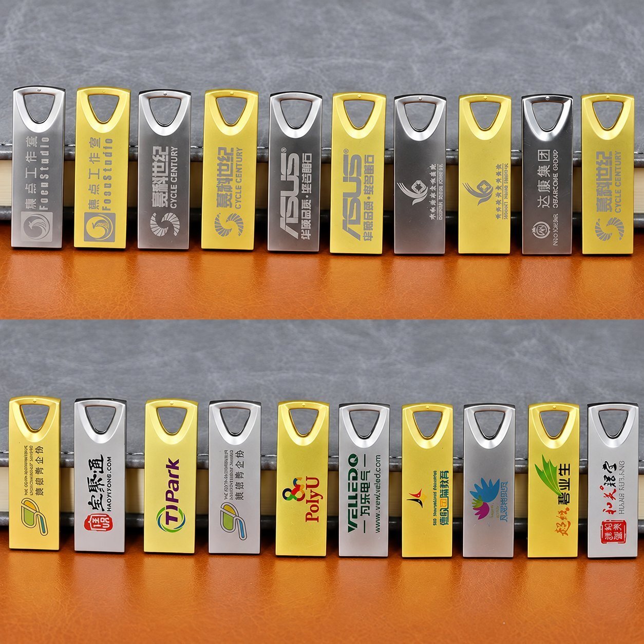 A row of yellow and silver metal USB flash drives with triangular lanyard cutouts, each laser-engraved with a different brand name and logo, illustrating full-color and engraved branding methods applied to a metal USB body.